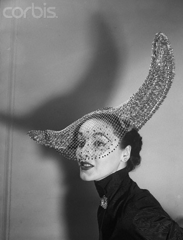 Original caption:1/11/52: High drama is achieved by Walter Florell in this rough grey straw with a soaring, cutaway brim. The white mesh veil is studded with red sequins.